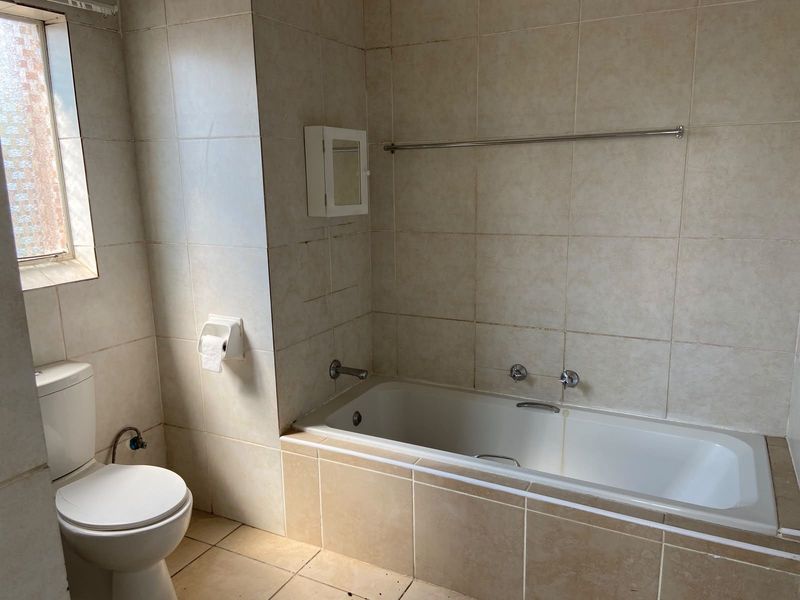 A functional bathroom featuring a built-in bathtub, toilet, and neutral wall tiling. The space is ready for cosmetic updates to improve its overall condition.