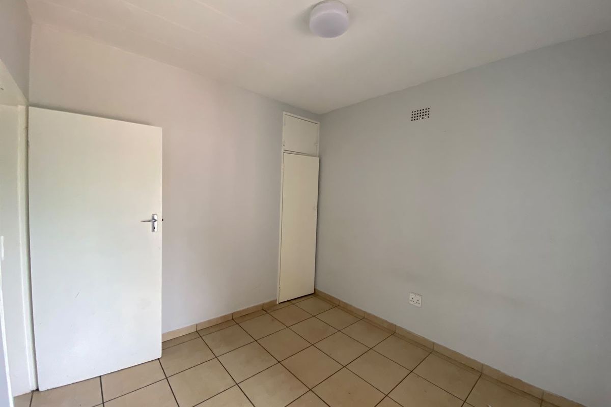 A vacant bedroom featuring neutral tiled flooring, a built-in cupboard, and a simple ceiling light fixture, offering a blank canvas for personalization.