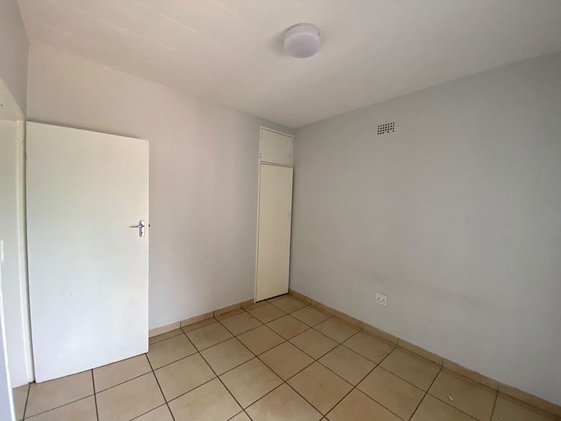 A vacant bedroom featuring neutral tiled flooring, a built-in cupboard, and a simple ceiling light fixture, offering a blank canvas for personalization.