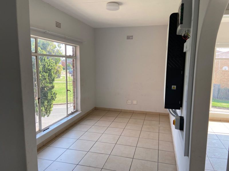 A bright, empty utility space featuring tiled flooring, a large window, and a wall-mounted solar inverter system.