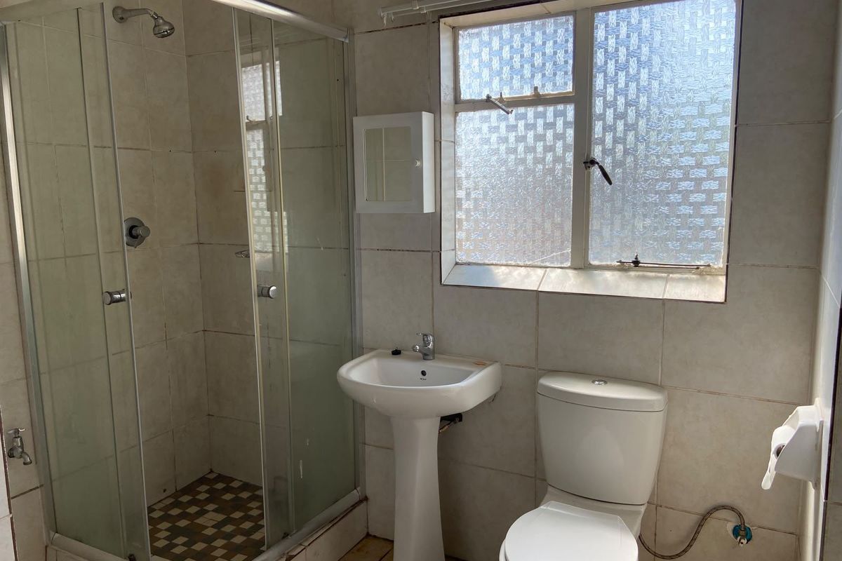 A functional bathroom featuring a shower enclosure, pedestal basin, and toilet with tiled finishes and an obscured glass window for privacy.