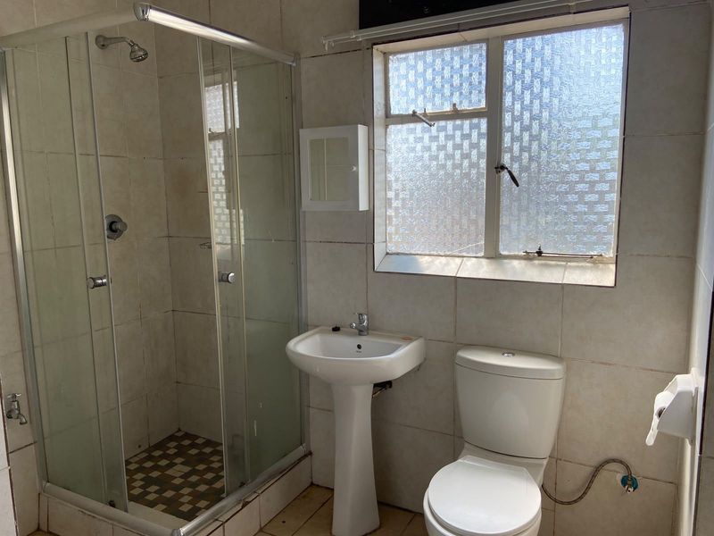 A functional bathroom featuring a shower enclosure, pedestal basin, and toilet with tiled finishes and an obscured glass window for privacy.