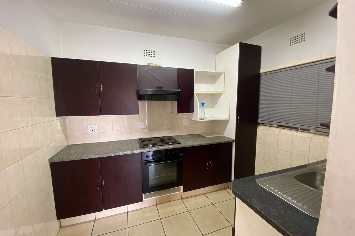 A functional kitchen featuring dark cabinetry, laminate countertops, built-in oven and hob, tiled splashbacks, and tiled flooring.