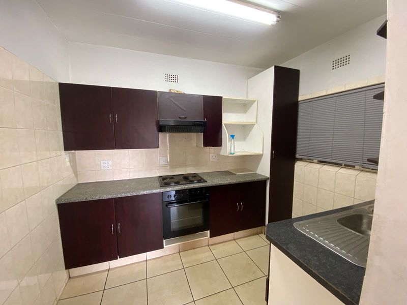 A functional kitchen featuring dark cabinetry, laminate countertops, built-in oven and hob, tiled splashbacks, and tiled flooring.