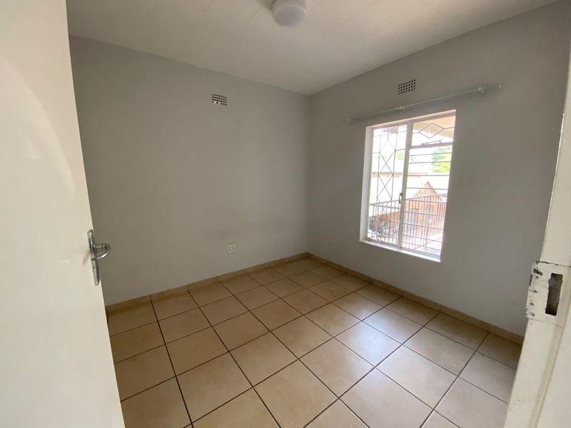 An empty bedroom featuring tiled flooring, a window with security bars, and neutral wall finishes, providing a blank canvas for personalization.