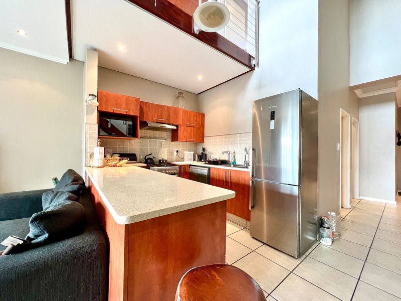 Open-plan kitchen featuring stone countertops, wooden cabinetry, and tiled flooring, seamlessly integrated with the living area under a mezzanine level.