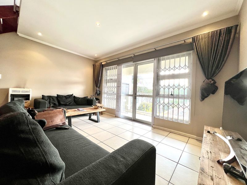 A bright living room featuring tiled flooring, recessed lighting, and a sliding glass door with security gate leading to an outdoor area.