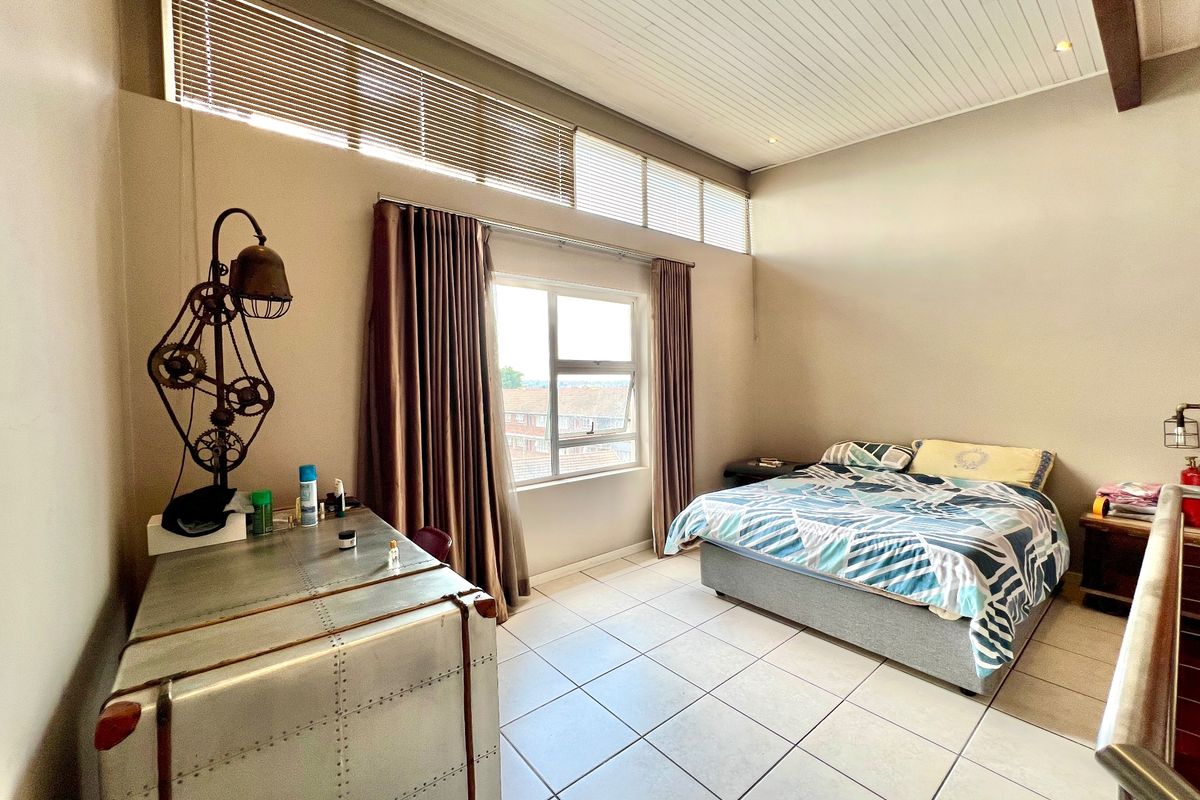Spacious bedroom featuring high-level clerestory windows, a unique tongue and groove ceiling, and neutral tiled flooring, offering a bright and airy atmosphere.