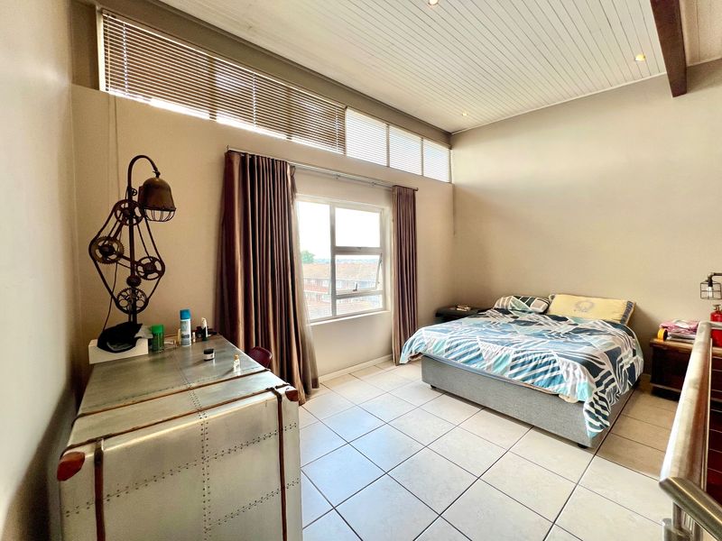 Spacious bedroom featuring high-level clerestory windows, a unique tongue and groove ceiling, and neutral tiled flooring, offering a bright and airy atmosphere.