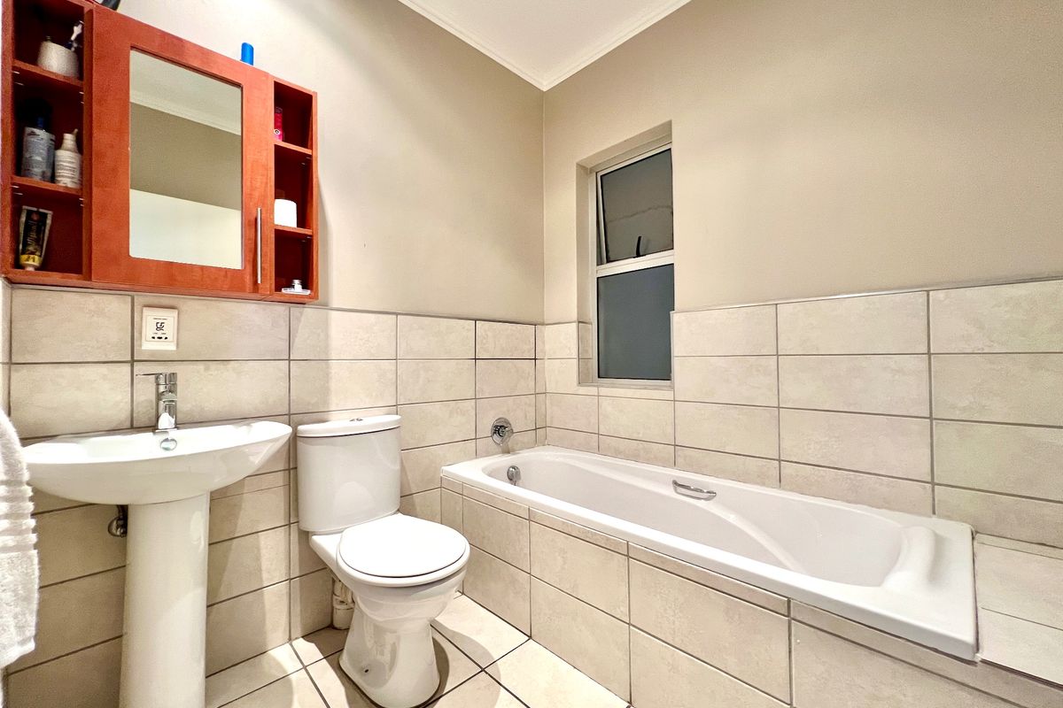 A functional bathroom featuring a pedestal basin, toilet, and a built-in bathtub with neutral wall and floor tiling.
