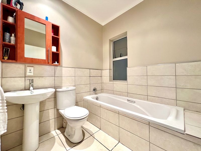 A functional bathroom featuring a pedestal basin, toilet, and a built-in bathtub with neutral wall and floor tiling.