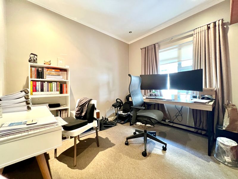 A functional home office space featuring neutral wall tones, carpeted flooring, and natural light provided by a window with installed curtain tracks.