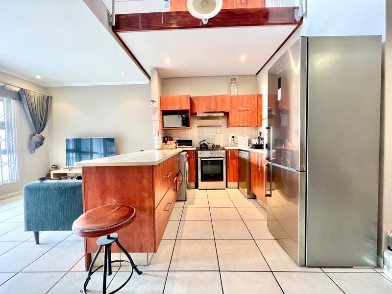 Open-plan kitchen and living area featuring wooden cabinetry, stone countertops, tiled flooring, and a breakfast bar, creating a functional and connected living space.