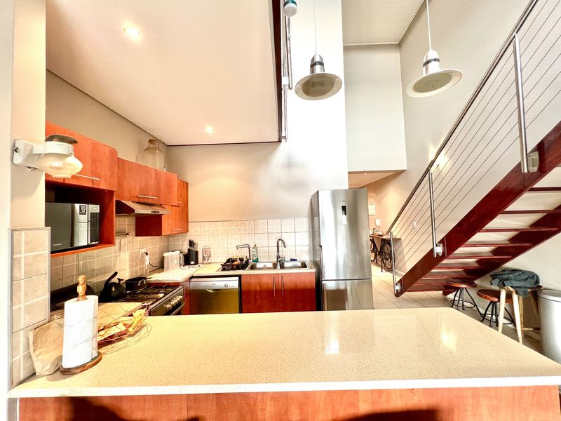Open-plan kitchen featuring wooden cabinetry, stone countertops, and integrated appliances, seamlessly connected to a staircase leading to the upper level.