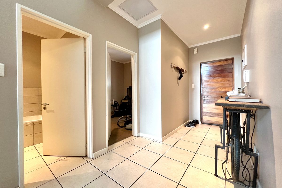 A bright and functional hallway featuring tiled flooring, recessed ceiling lighting, and a solid wood front door providing access to adjacent rooms.