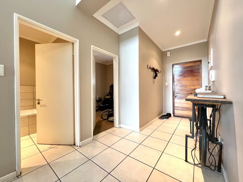 A bright and functional hallway featuring tiled flooring, recessed ceiling lighting, and a solid wood front door providing access to adjacent rooms.