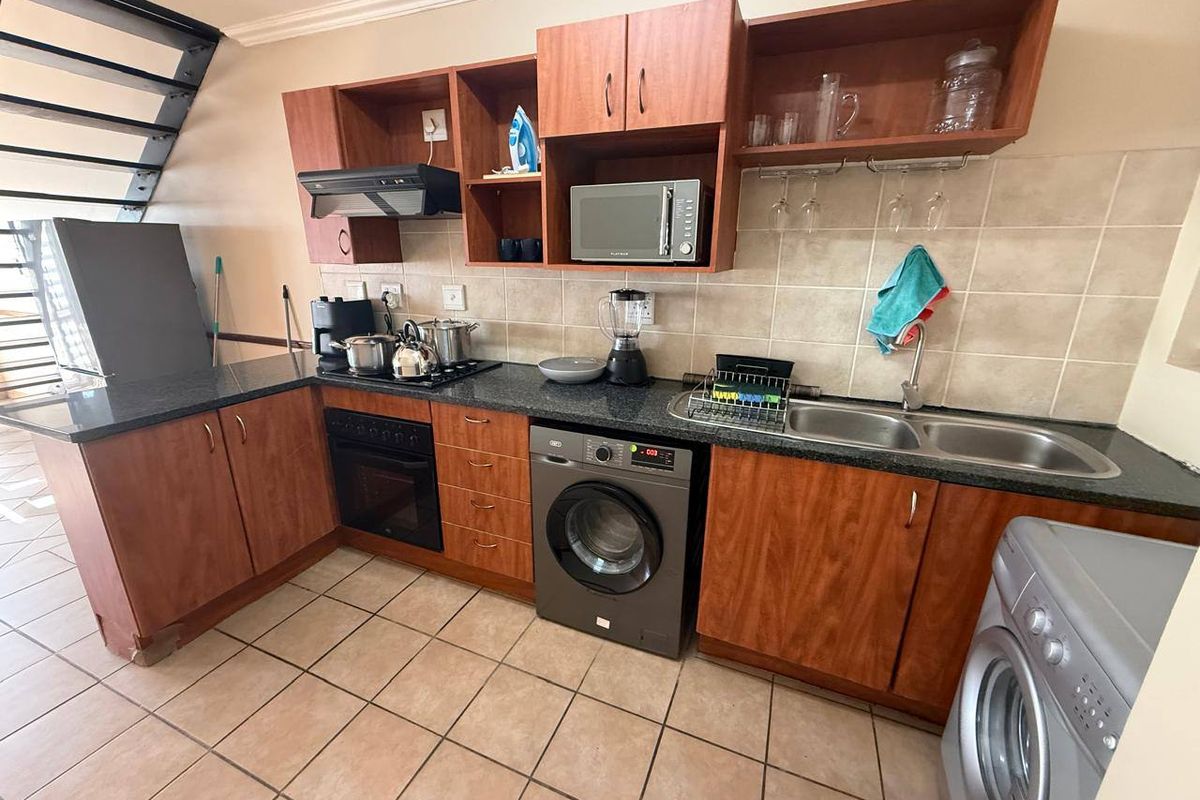 Functional kitchen featuring laminate cabinetry, granite countertops, double basin sink, built-in oven, hob, and extractor fan with tiled flooring and backsplash.
