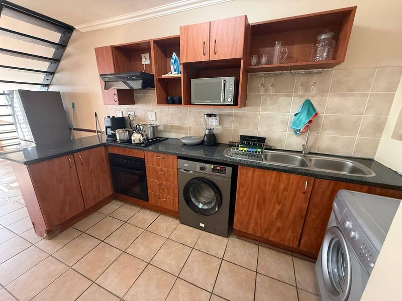 Functional kitchen featuring laminate cabinetry, granite countertops, double basin sink, built-in oven, hob, and extractor fan with tiled flooring and backsplash.