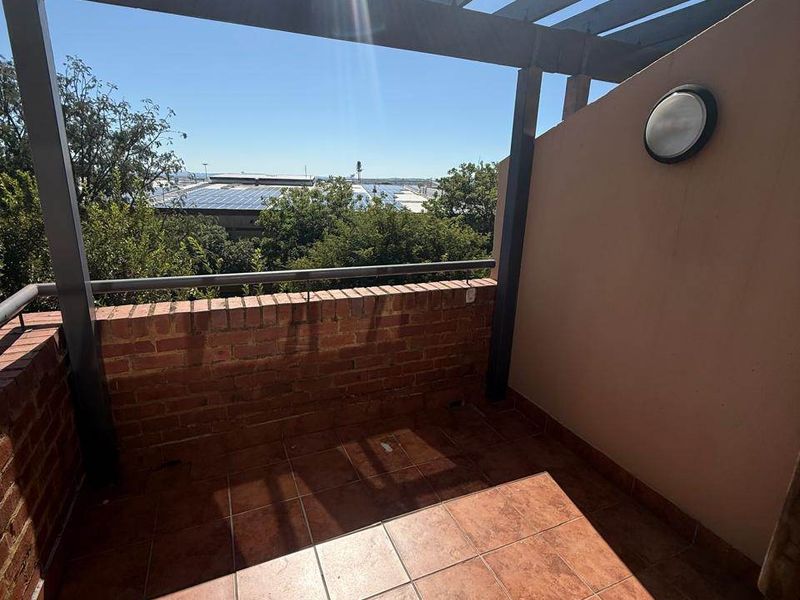 A private balcony featuring a timber pergola, brick balustrade, and tiled flooring, offering an open outdoor space with a view.