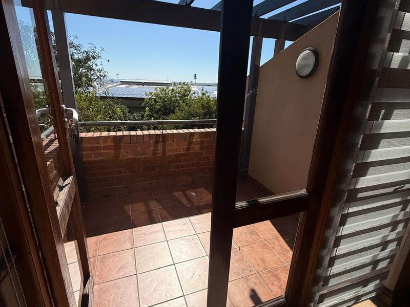 A private balcony featuring a timber pergola, brick balustrade, and tiled flooring, offering an outdoor space accessible through a timber-framed glass door.