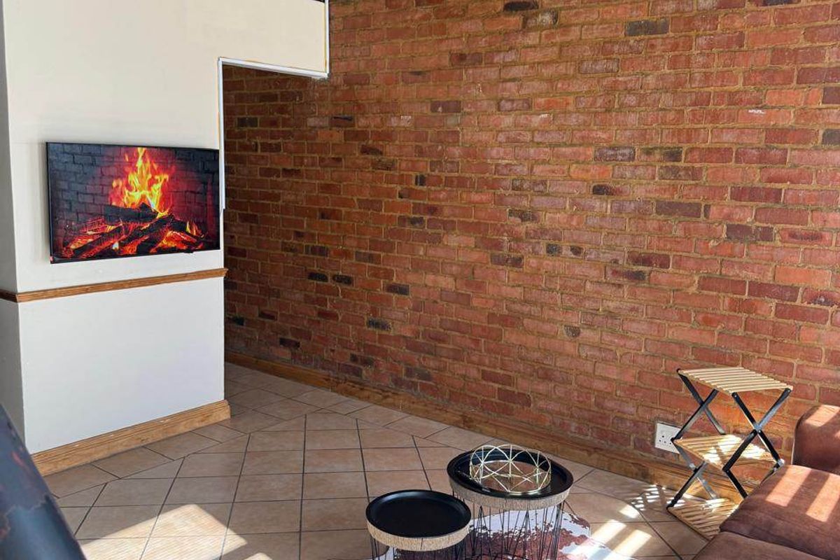 A double-volume living area featuring an exposed brick feature wall, tiled flooring, and a mezzanine level with a metal railing.