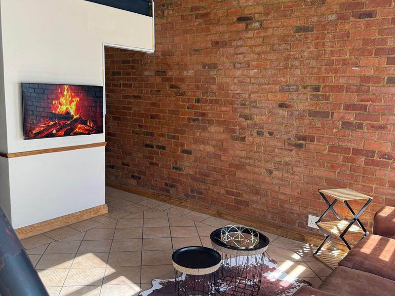 A double-volume living area featuring an exposed brick feature wall, tiled flooring, and a mezzanine level with a metal railing.
