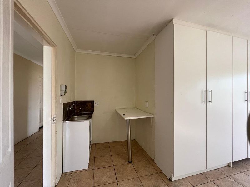 A compact scullery or utility area featuring built-in storage cupboards, a stainless steel sink, and a wall-mounted prep counter with tiled flooring.