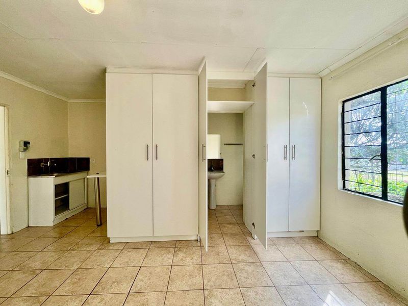 A functional bedroom featuring built-in cupboards, tiled flooring, and an integrated en-suite basin area with security bars on the window.