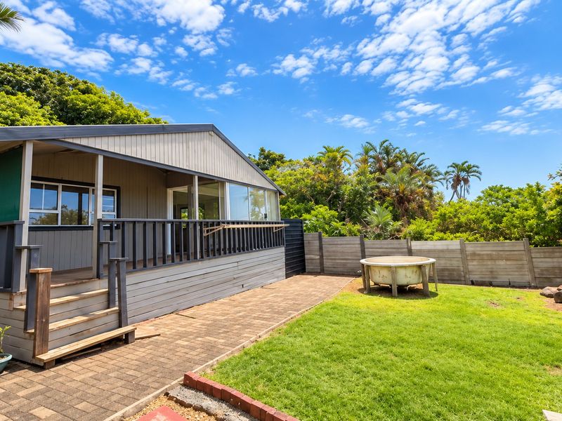 Rear view of the property featuring a covered timber deck, paved patio area, and a private garden enclosed by a concrete boundary wall.