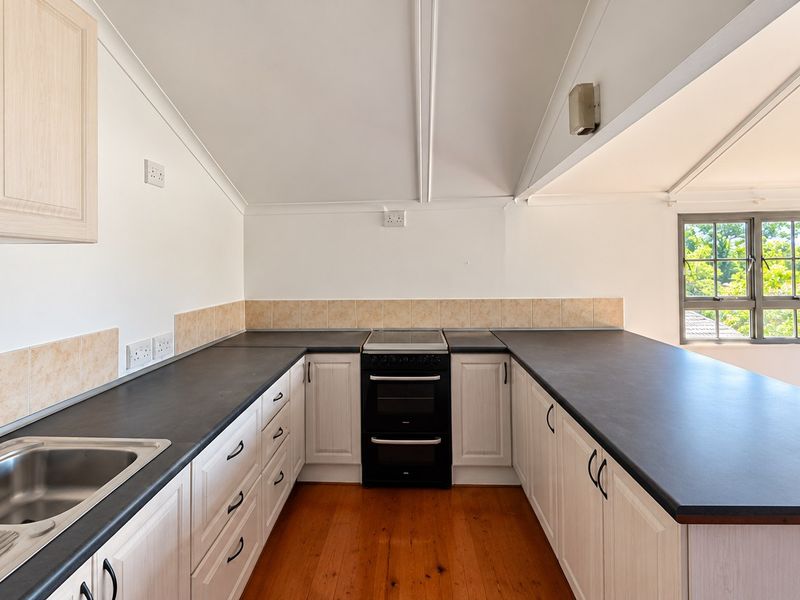 A clean, functional kitchen featuring light-toned cabinetry, dark countertops, a stainless steel sink, and a freestanding oven, set against a bright, pitched-ceiling space.