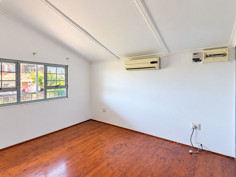 A bright, empty bedroom featuring laminate flooring, a split-system air conditioner, and a large sliding window.