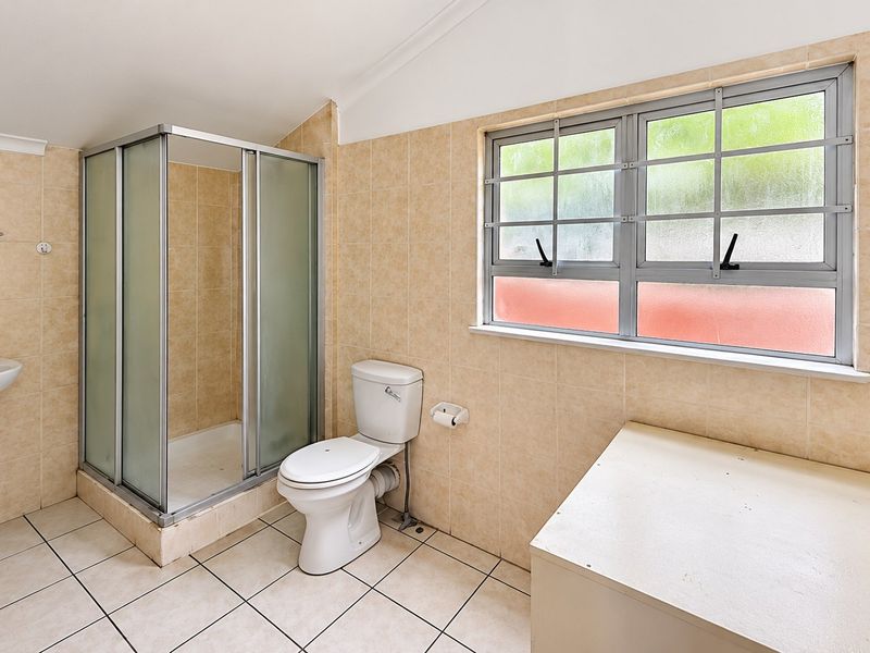 A functional bathroom featuring a pedestal basin, shower enclosure, and toilet, finished with neutral wall and floor tiles.