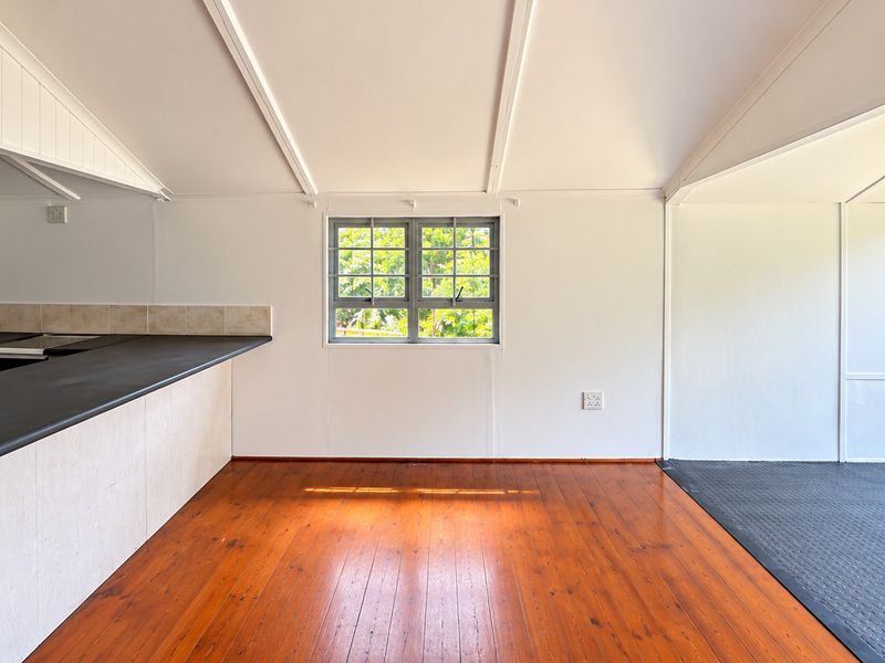 An open-plan living and kitchen area featuring polished timber flooring, neutral walls, and a functional kitchen layout with direct access to an outdoor balcony.