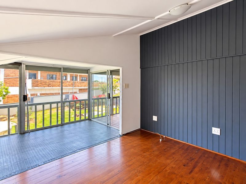 Spacious living area featuring polished timber flooring, a striking dark vertical paneled feature wall, and large sliding glass doors opening to an outdoor balcony.