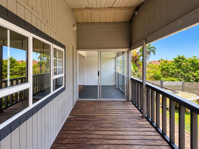 A covered timber deck patio featuring a balustrade and sliding glass door access to the interior, overlooking a private garden area.
