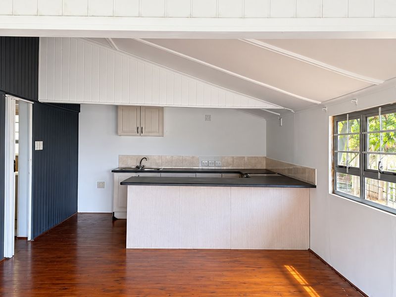 An open-plan living and kitchen area featuring timber flooring, vaulted ceilings, and a functional kitchen layout with ample counter space and cabinetry.