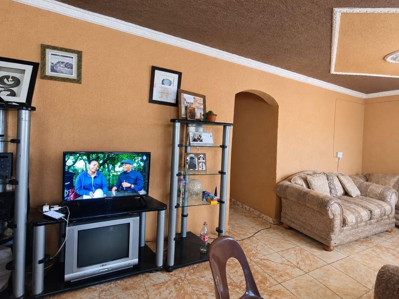 A living room featuring tiled flooring, decorative ceiling molding, and an arched doorway leading to another area of the home.