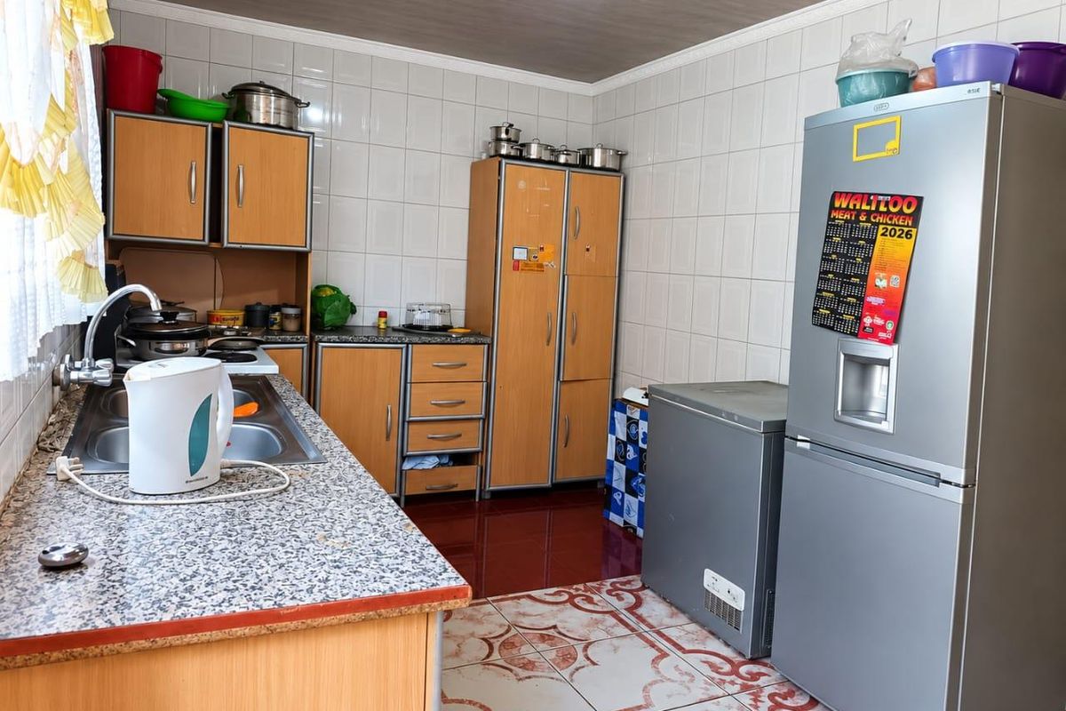 A functional kitchen featuring laminate cabinetry, granite-look countertops, stainless steel sink, and tiled finishes throughout.