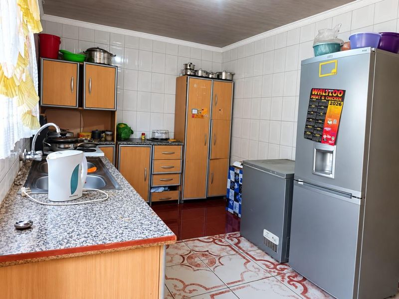 A functional kitchen featuring laminate cabinetry, granite-look countertops, stainless steel sink, and tiled finishes throughout.