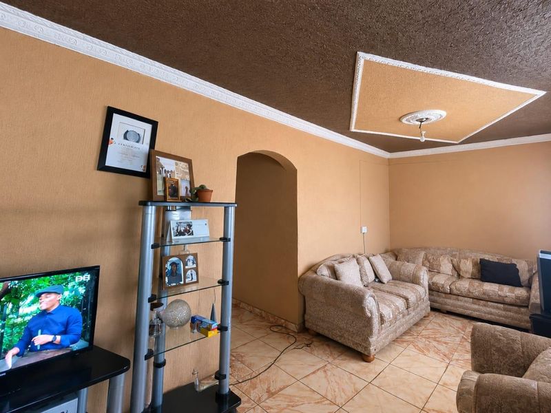 A living room featuring tiled flooring, decorative ceiling molding, and an arched doorway leading to an adjacent space.