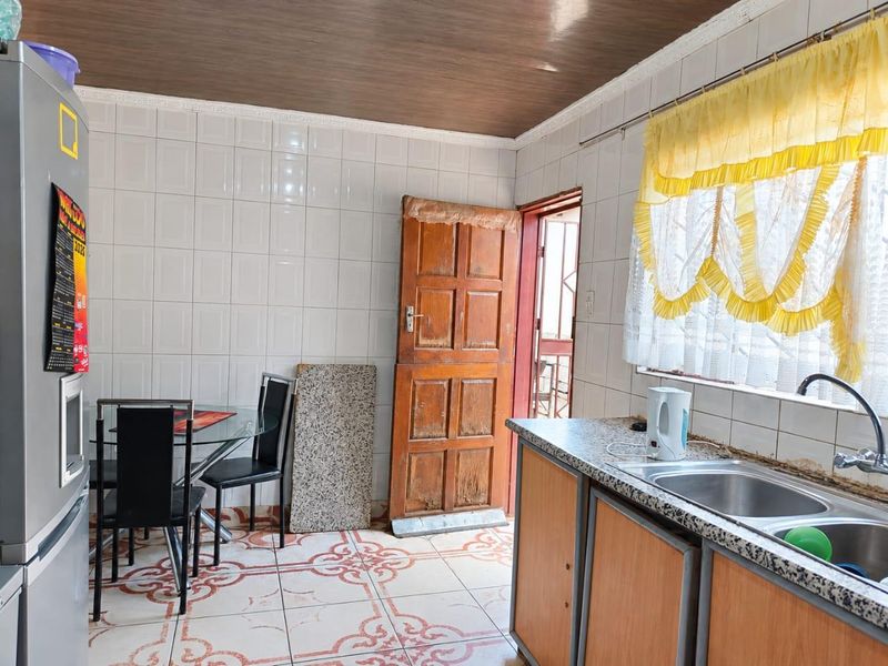 A functional kitchen featuring laminate cabinetry, a double bowl sink, and tiled surfaces, offering potential for a modern renovation.