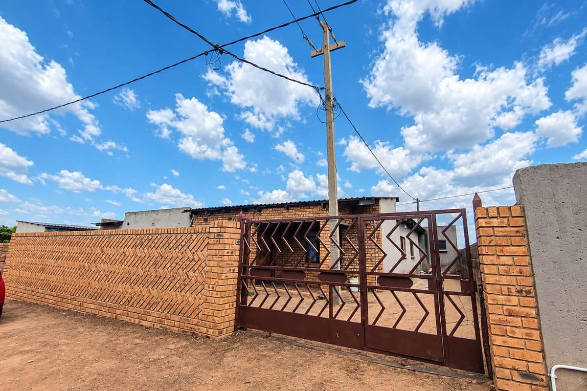 Front view of the property featuring a decorative brick boundary wall and a secure metal driveway gate.