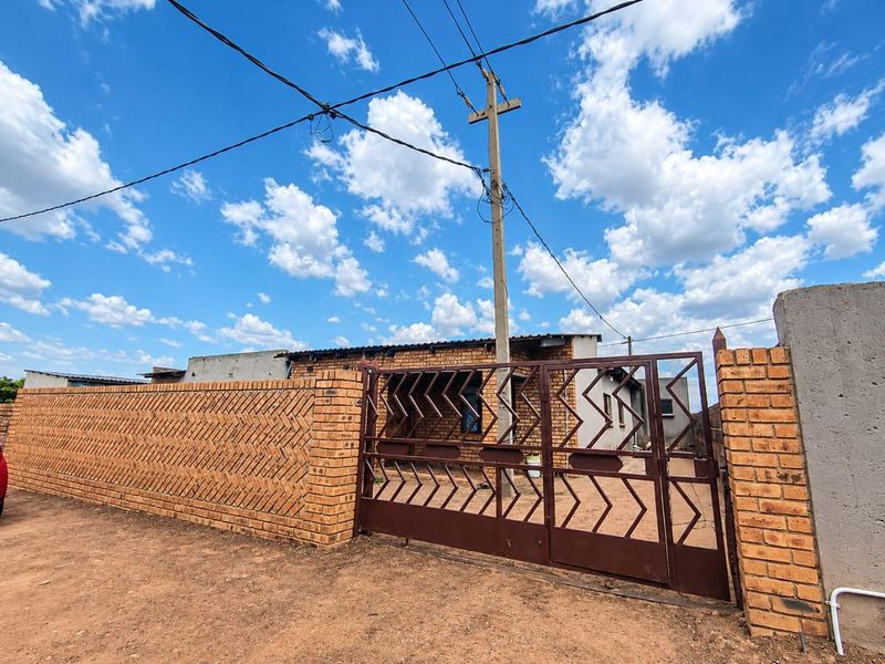 Front view of the property featuring a decorative brick boundary wall and a secure metal driveway gate.
