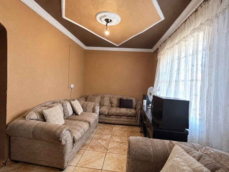 A living room featuring ceramic floor tiles, decorative ceiling coving, and a central ceiling rose.