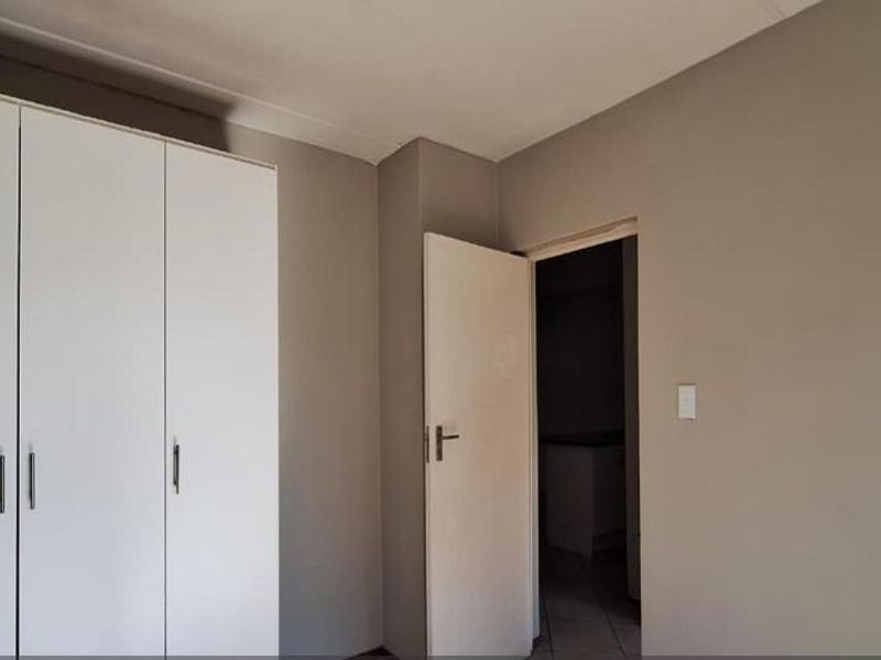 A clean, empty bedroom featuring neutral wall paint and a functional built-in wardrobe with white doors.