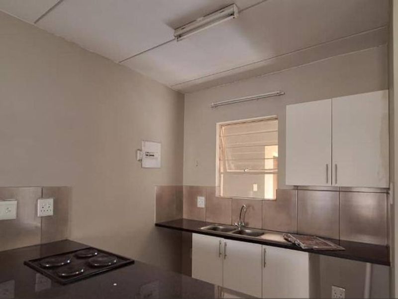 A functional kitchen featuring built-in cabinetry, dark laminate countertops, a stainless steel sink, and a built-in electric hob with a tiled backsplash.
