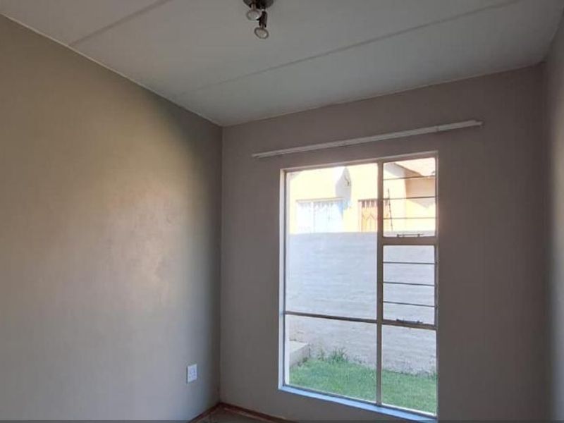 A vacant bedroom featuring neutral walls, a large window with security bars, and a simple ceiling light fixture, ready for personalization.
