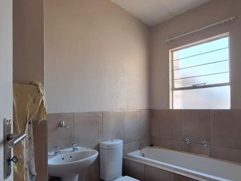 A functional bathroom featuring a pedestal basin, toilet, and bathtub with tiled splashbacks and a window providing natural light.