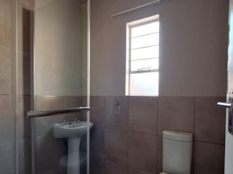A functional bathroom featuring a shower enclosure, pedestal basin, and toilet with neutral wall tiling.