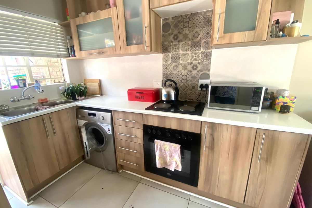 Functional kitchen featuring wood-look cabinetry, laminate countertops, built-in oven and hob, tiled splashback, and integrated space for a washing machine.